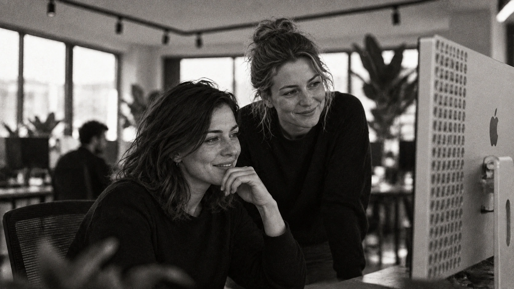 Two designers in black tops sharing a smile as they work at an Apple Pro Display XDR in the Designco studio