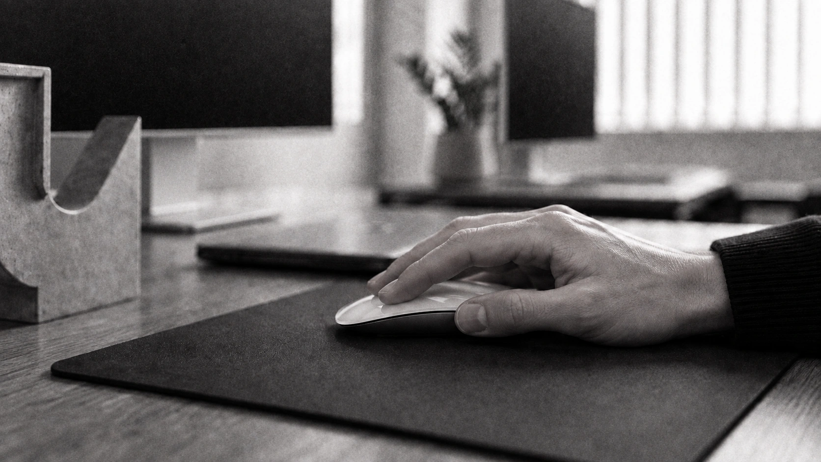 A hand using a mouse at a Designco workstation, with the studio softly out of focus