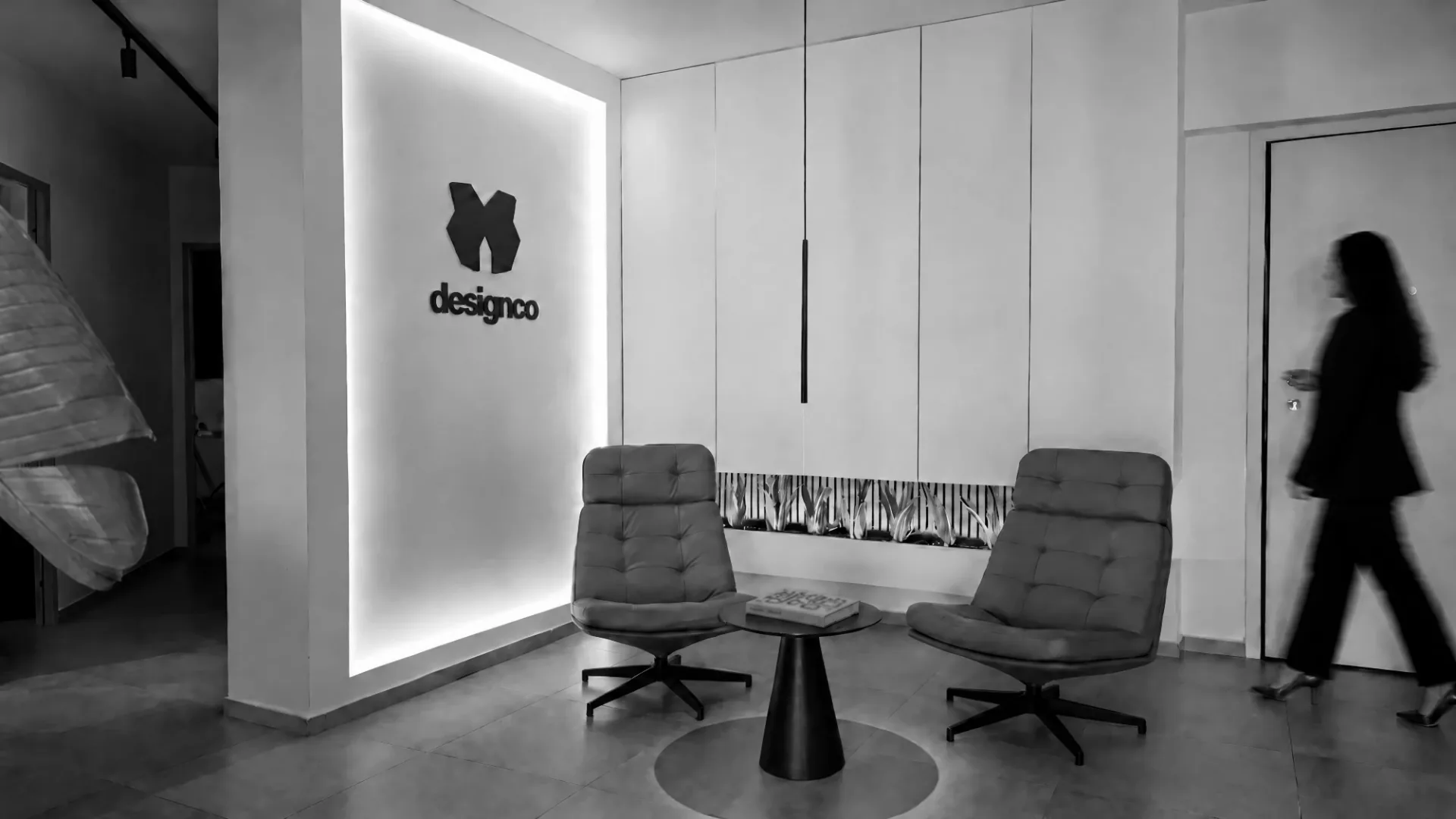 A colleague walking past the backlit Designco mark in the studio reception