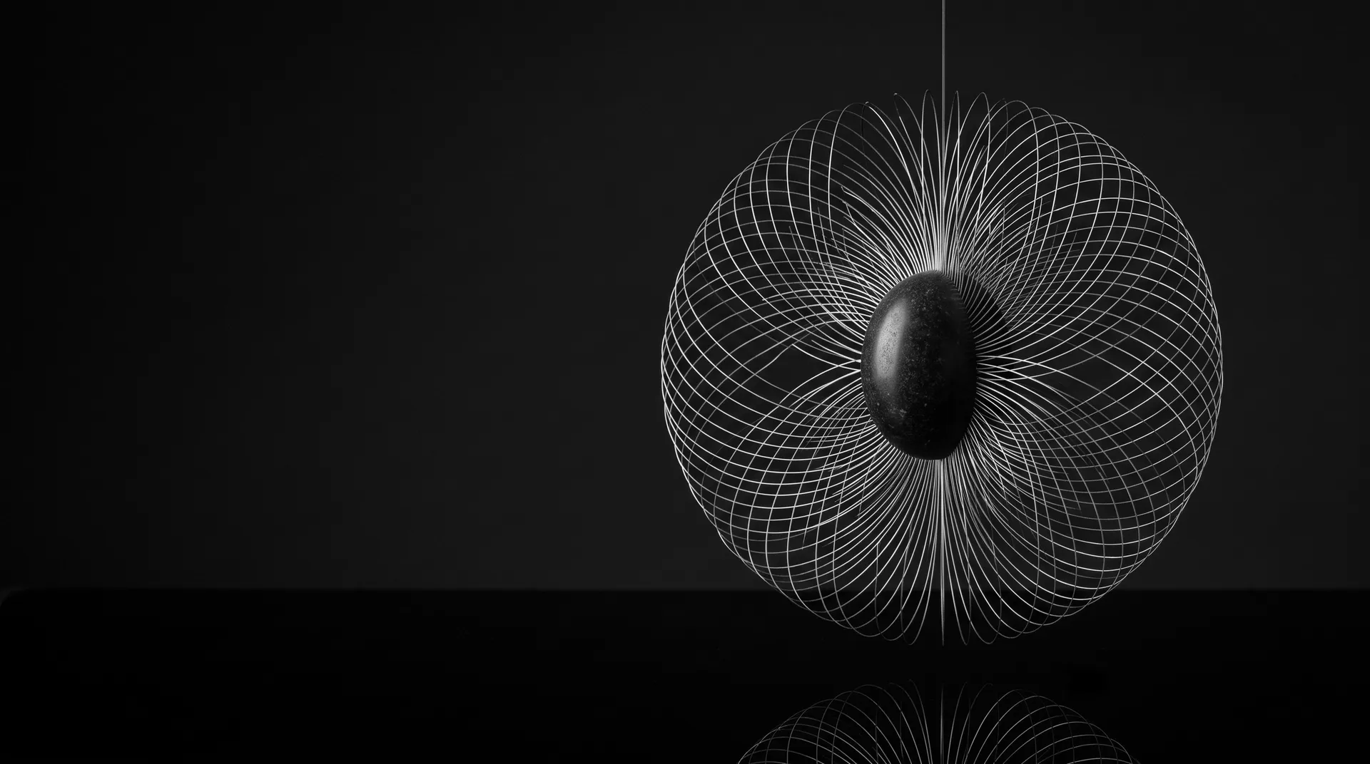 A dark polished stone core suspended inside a sphere of fine silver filaments against black