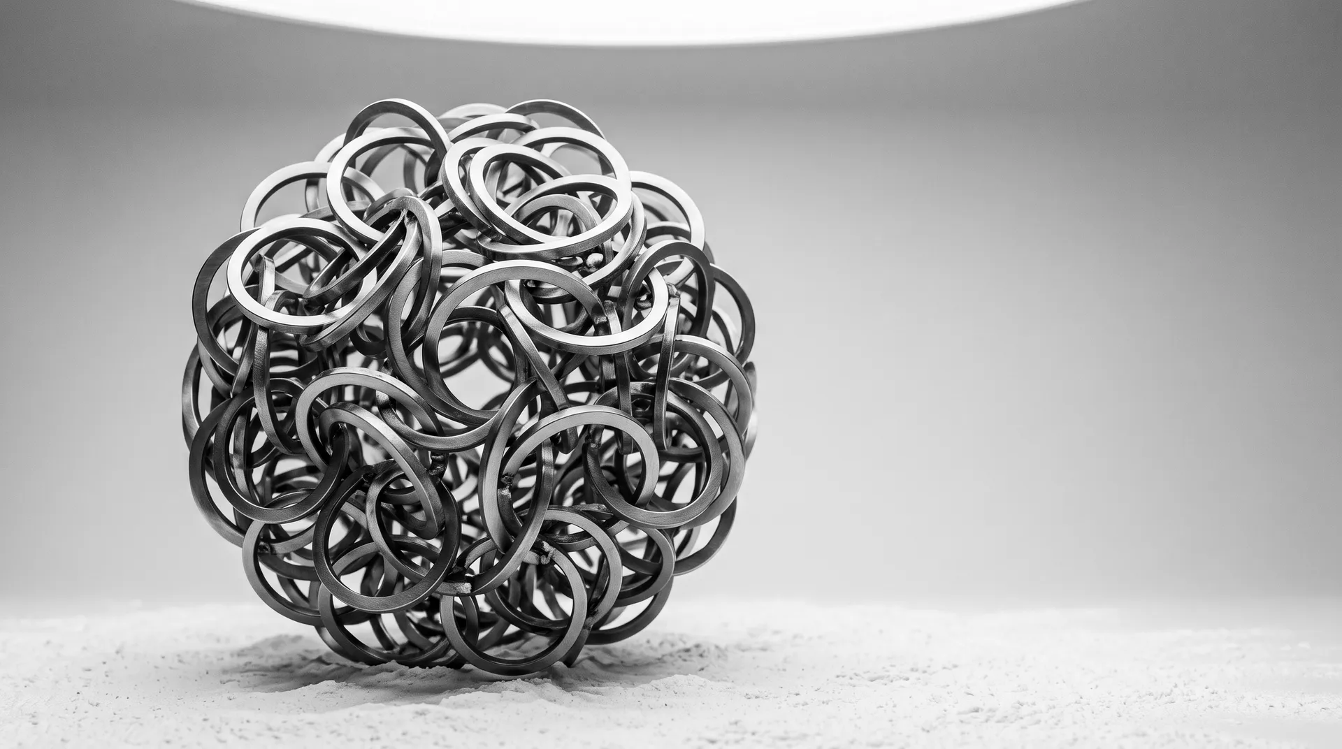 Hundreds of brushed-steel rings interlinked into one continuous sphere on a white powder floor