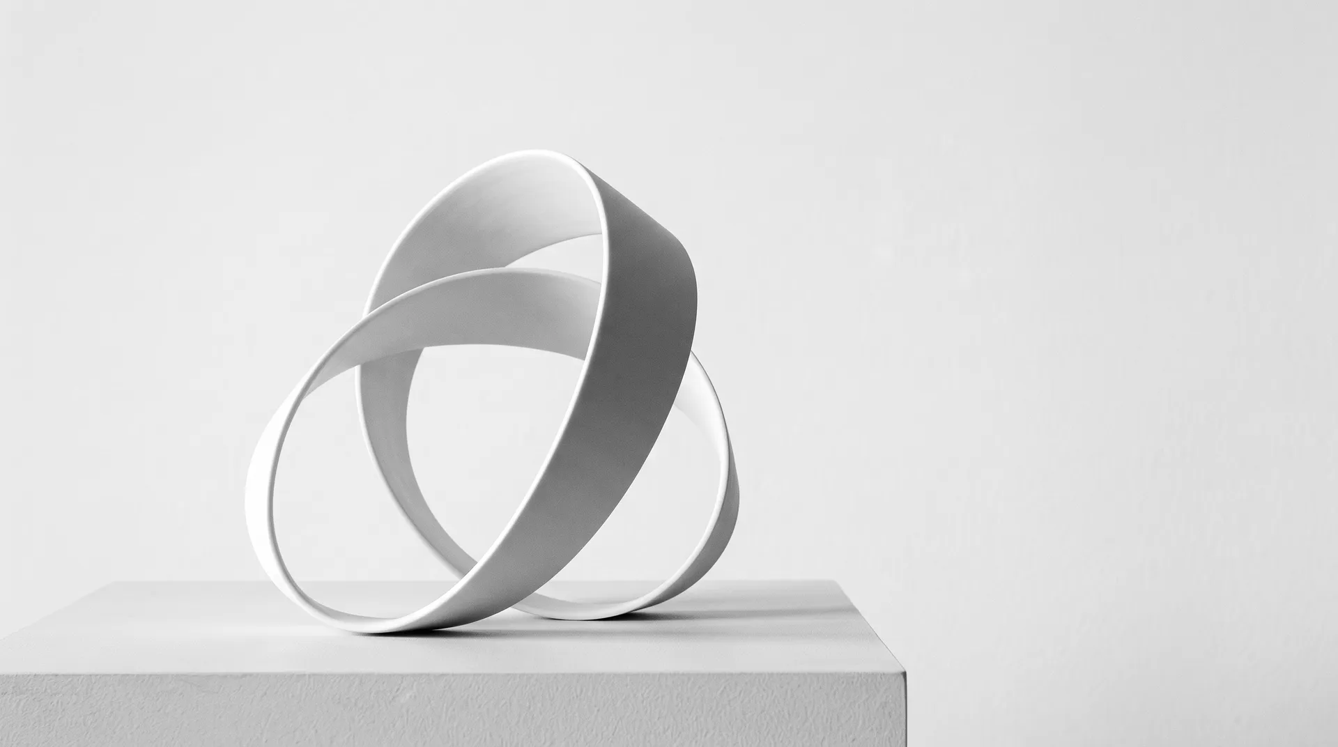 One continuous ribbon of matte white porcelain folded into a calm loop on a pale plinth